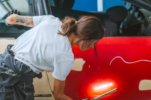A young woman mechanic checks a car door with a flashlight to paint it. Concept of equality