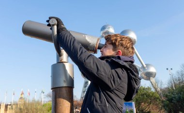 Genç bir çocuk dev bir teleskoptan bakar. Arkaplanda Brüksel atomu