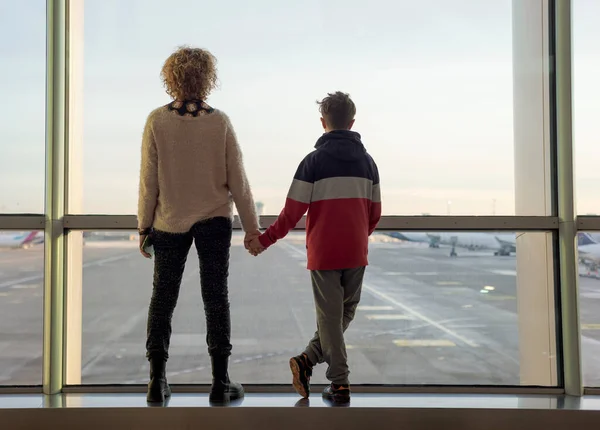 妈妈和十多岁的儿子从机场的窗户往外看 — 图库照片