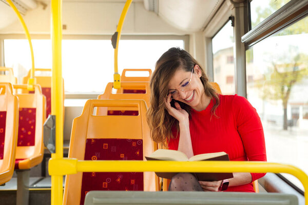 A young woman smiles reading a book on the public bus.