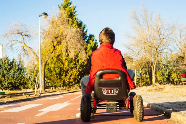 Kırmızı yelekli bir çocuk trafik parkında pedallı go-kart kullanıyor.