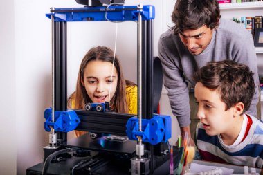 Mutlu çocuklar, genç bir yetişkinle 3D baskı yapmayı öğreniyor.