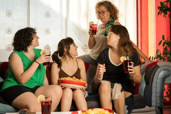 Friends having fun during a party on the sofa, eating snacks and drinking soft drinks.