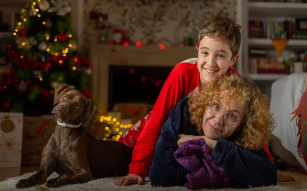 Mom and son lying on the floor with their dog in front of the fireplace at Christmas. Family Christmas concept
