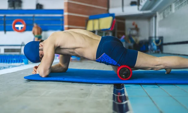 A young swimmer stretches with a rollerball before training in the pool. Concept of healthy living and self-improvement