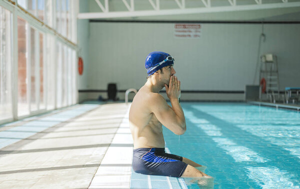A swimmer with cap and goggles sitting at the edge of the pool.