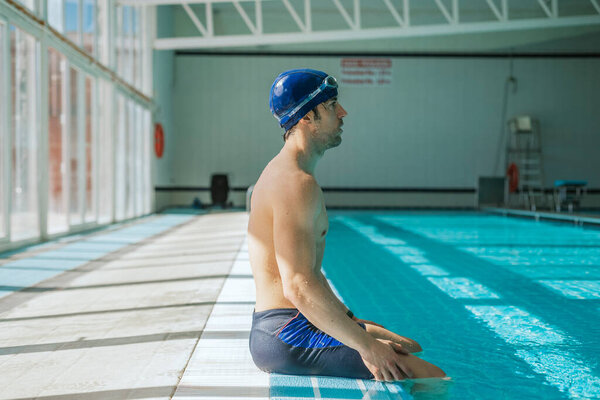 A swimmer with cap and goggles sitting at the edge of the pool.