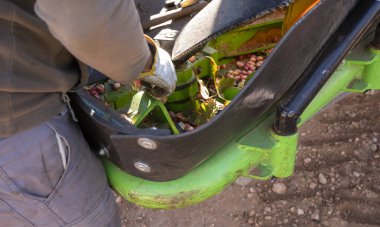 Bir tarımsal şam fıstığı biçme makinesinin bakımını yapan bir operatörün elleri yakın plan..