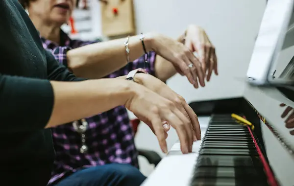 Close-up of the piano teacher\'s hands placing the hands of her pupil