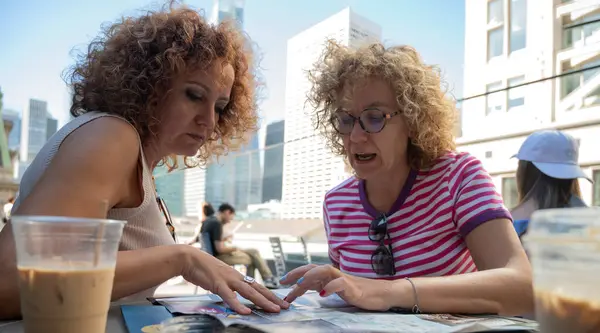 Two Women Discussing City Map Sunny Rooftop Cafe Urban Skyline Stock Image