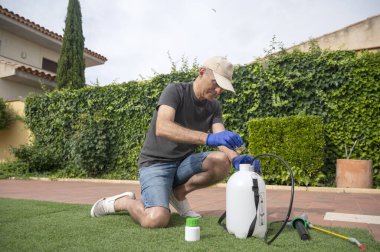 Koruyucu eldivenleri ve kepiyle bahçede böcek ilacı hazırlayan orta yaşlı bir adam.