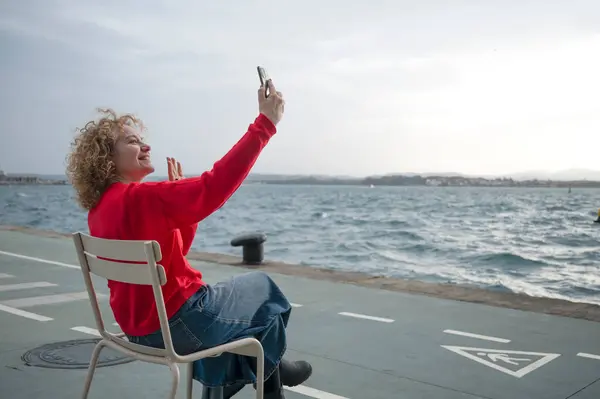 Bulutlu bir günde deniz kenarında selfie çeken bir kadın.