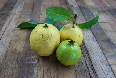 Ahşap arka planda yeşil yapraklı taze kırmızı guava. Ahşap ve guava yapraklarının dokusu.