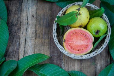 Örülmüş bambu sepetinde taze kırmızı guava ve ahşap arka planda yeşil yapraklar. Ahşap ve guava yapraklarının dokusu.