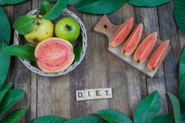 Örülmüş bambu sepetinde taze kırmızı guava ve ahşap arka planda yeşil yapraklar. Ahşap ve guava yapraklarının dokusu.