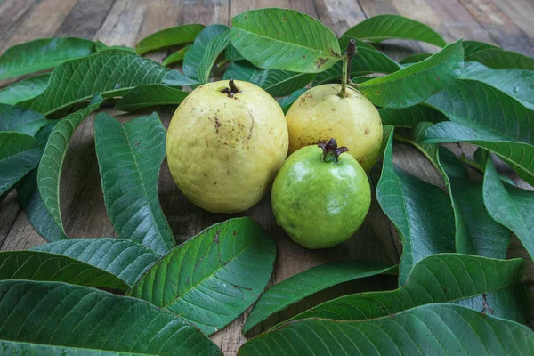 Ahşap arka planda yeşil yapraklı taze kırmızı guava. Ahşap ve guava yapraklarının dokusu.