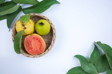 Örülmüş bambu sepetinde taze kırmızı guava ve beyaz arka planda yeşil yapraklar.
