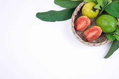 Örülmüş bambu sepetinde taze kırmızı guava ve beyaz arka planda yeşil yapraklar.