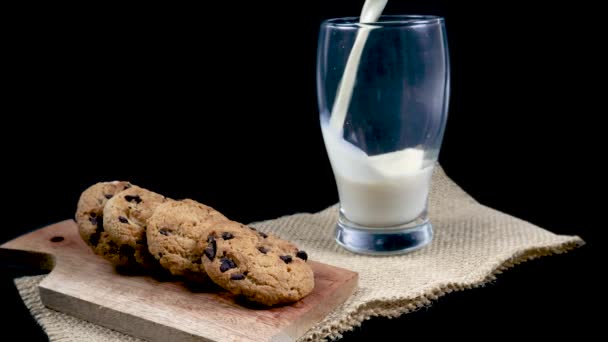 黒い背景にチョコレートチップクッキーとガラスに新鮮なミルクを注ぐ — ストック動画