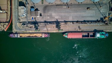 Tahıl ambarlarından limandaki deniz kargo gemisinin ambarlarına tahıl yüklüyorlar. Kuru kargo gemisinin tahıllı sığınağı. Havadan üst görünüm.