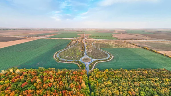 Güzel bir sonbahar ormanında dairesel yol kesişiminde hava manzarası. Sonbaharda yuvarlak kavşağın havadan görünüşü.