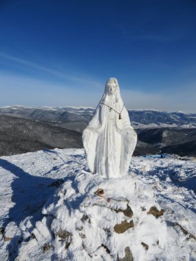 Madonna kışın dağlarda, kayak yamacında ve sandalyede, dağlardaki kış ormanlarının arasında köy manzarası