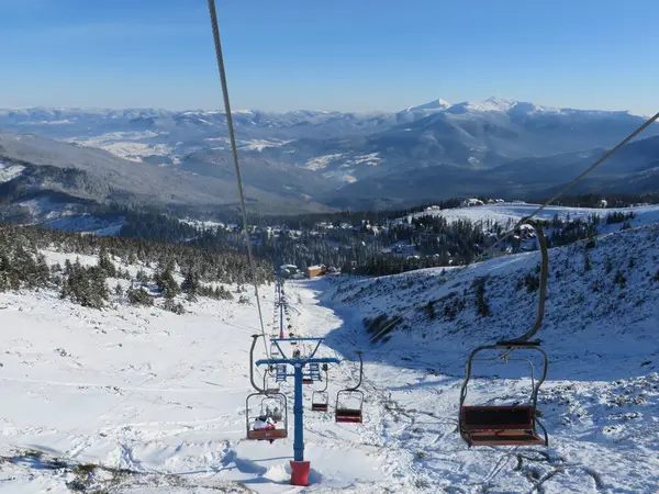 Kışın dağlar, kayak yamaçları ve teleferik, dağlardaki kış ormanlarının arasındaki köy manzarası.