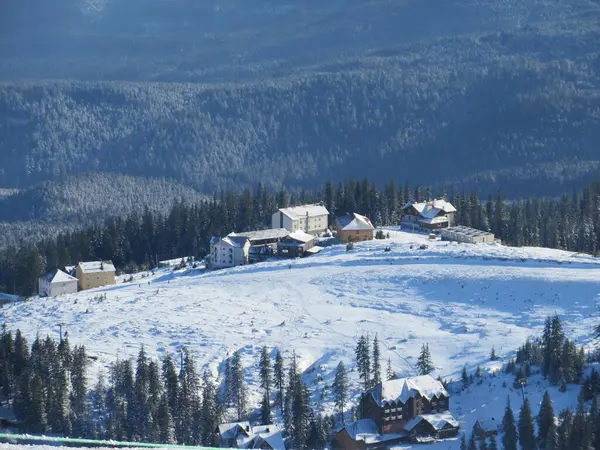Kışın dağlar, kayak yamaçları ve teleferik, dağlardaki kış ormanlarının arasındaki köy manzarası.