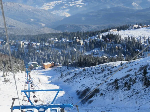 Kışın dağlar, kayak yamaçları ve teleferik, dağlardaki kış ormanlarının arasındaki köy manzarası.