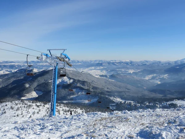 Kışın dağlar, kayak yamaçları ve teleferik, dağlardaki kış ormanlarının arasındaki köy manzarası.