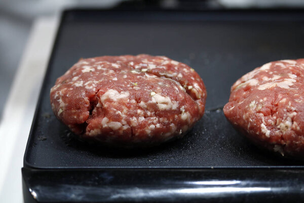 raw round burger meat on griddle prepared for cooking