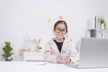 Küçük iş kadını Asya. Gözlüklü ve resmi giysili şirin kız masada oturuyor ve dizüstü bilgisayar kullanıyor.