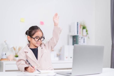 Küçük iş kadını Asya. Gözlüklü ve resmi giysili şirin kız masada oturuyor ve dizüstü bilgisayar kullanıyor.
