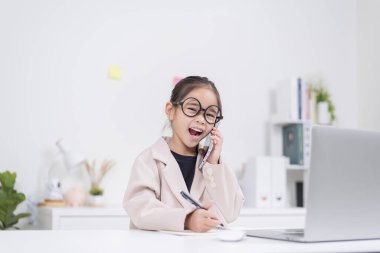 Küçük iş kadını Asya. Gözlüklü ve resmi giysili şirin kız masada oturuyor ve dizüstü bilgisayar kullanıyor.