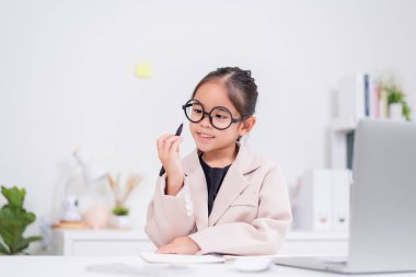 Küçük iş kadını Asya. Gözlüklü ve resmi giysili şirin kız masada oturuyor ve dizüstü bilgisayar kullanıyor.