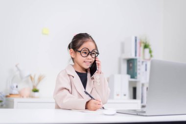 Küçük iş kadını Asya. Gözlüklü ve resmi giysili şirin kız masada oturuyor ve dizüstü bilgisayar kullanıyor.