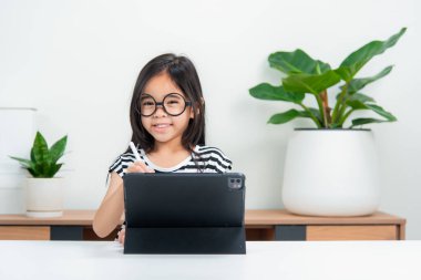 Asyalı çocuk öğrenci video karşısında heyecanlanmış online ders çalışmayı öğreniyor ya da evden tabletle öğreniyor.