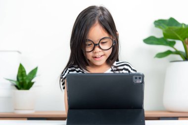Asyalı çocuk öğrenci video karşısında heyecanlanmış online ders çalışmayı öğreniyor ya da evden tabletle öğreniyor.