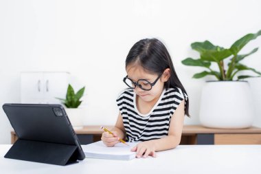 Asyalı çocuk öğrenci video karşısında heyecanlanmış online ders çalışmayı öğreniyor ya da evden tabletle öğreniyor.