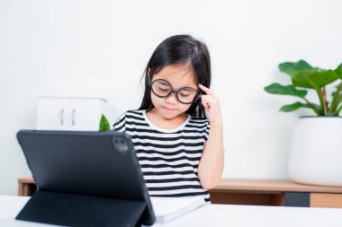 Asyalı çocuk öğrenci video karşısında heyecanlanmış online ders çalışmayı öğreniyor ya da evden tabletle öğreniyor.