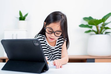 Asyalı çocuk öğrenci video karşısında heyecanlanmış online ders çalışmayı öğreniyor ya da evden tabletle öğreniyor.