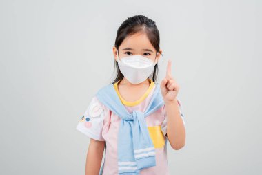 Koronavirüs salgınını korumak için maske takan Asyalı küçük kız çocuğu ve boş bir arkaplanı işaret eden yeni virüs Covid-19. 