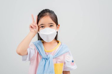 Koronavirüs salgınını korumak için maske takan Asyalı küçük kız çocuğu ve boş bir arkaplanı işaret eden yeni virüs Covid-19. 