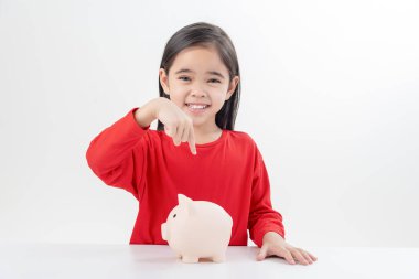 Küçük Asyalı kız domuz kumbarasında para biriktiriyor, tasarruf yapmayı öğreniyor, çocuk gelecek eğitim için para biriktiriyor. Para, finans, sigorta ve insan konsepti