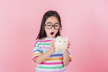 Küçük Asyalı kız domuz kumbarasında para biriktiriyor, tasarruf yapmayı öğreniyor, çocuk gelecek eğitim için para biriktiriyor. Para, finans, sigorta ve insan konsepti