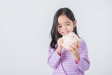 Küçük Asyalı kız domuz kumbarasında para biriktiriyor, tasarruf yapmayı öğreniyor, çocuk gelecek eğitim için para biriktiriyor. Para, finans, sigorta ve insan konsepti