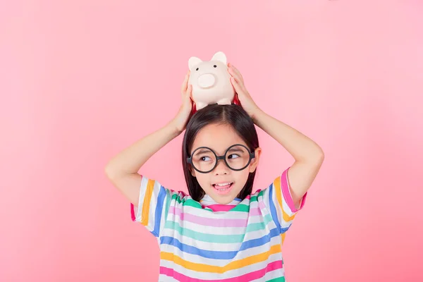 Little Asian girl saving money in a piggy bank, learning about saving, Kid save money for future education. Money, finances, insurance, and people concept