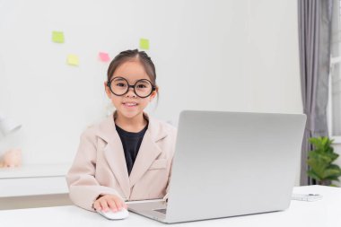 Küçük iş kadını Asya. Gözlüklü ve resmi giysili şirin kız masada oturuyor ve dizüstü bilgisayar kullanıyor.