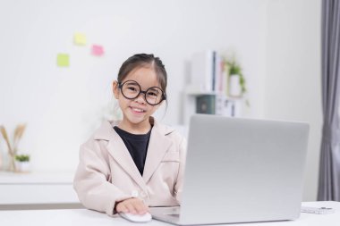Küçük iş kadını Asya. Gözlüklü ve resmi giysili şirin kız masada oturuyor ve dizüstü bilgisayar kullanıyor.