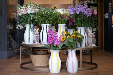 Çeşitli taze kesilmiş Matthiola incana veya stok çiçekleri, mini ayçiçekleri, Matricaria chamomilla veya papatya çiçekleri, Yunan çiçekçisinin beyaz vazolarındaki kalla zambakları - bahar zamanı. Yatay.